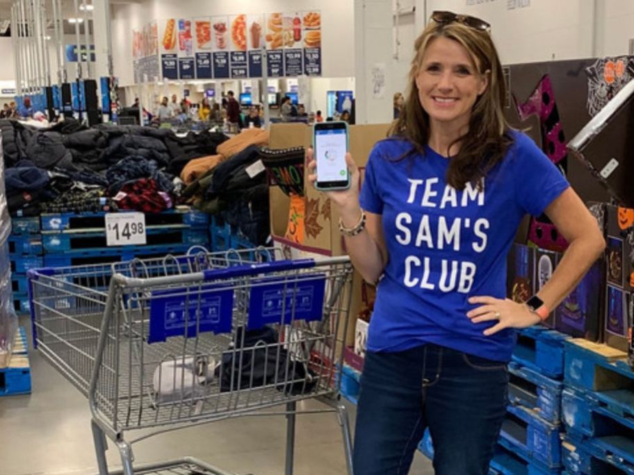 woman wearing a Team Sam's Club T-Shirt while holding up her phone next to a Sam's Club shopping cart