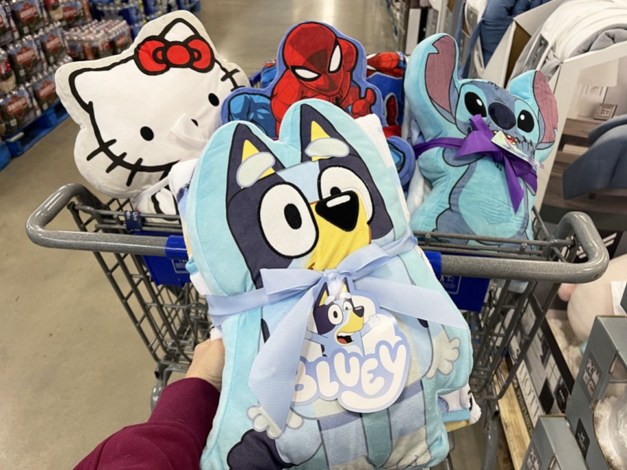 holding Bluey pillow & throw set in front of cart with Hello Kitty, Spider-Man and Stitch sets