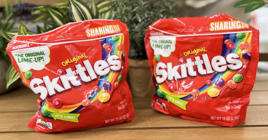 two large red bags of skittles candies on wood table