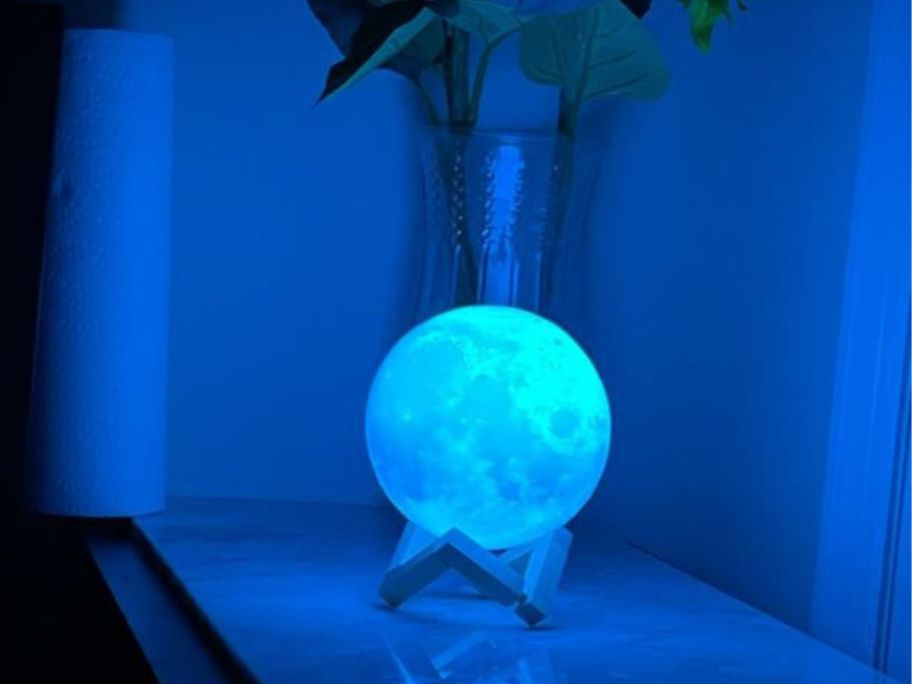 A small moon lamp woth a blue tint in front of a vase