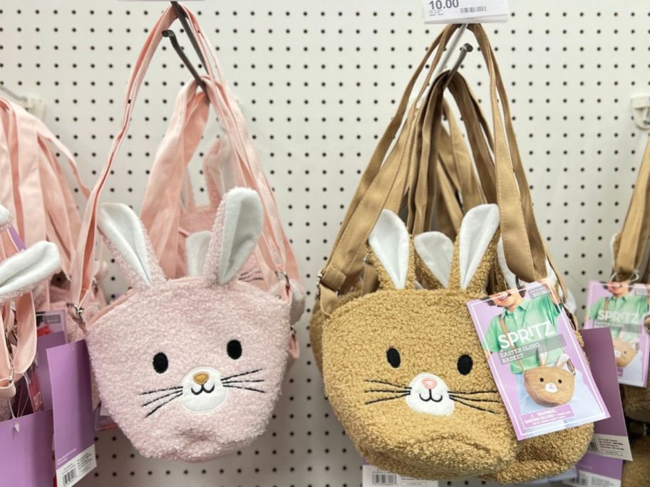 2 Spritz Easter Crossbody Terry Bags in pink and brown hanging on hooks in a Target store
