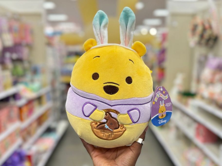 A person holding a Squishmallows Easter Disney Winnie the Pooh in Bunny Suit