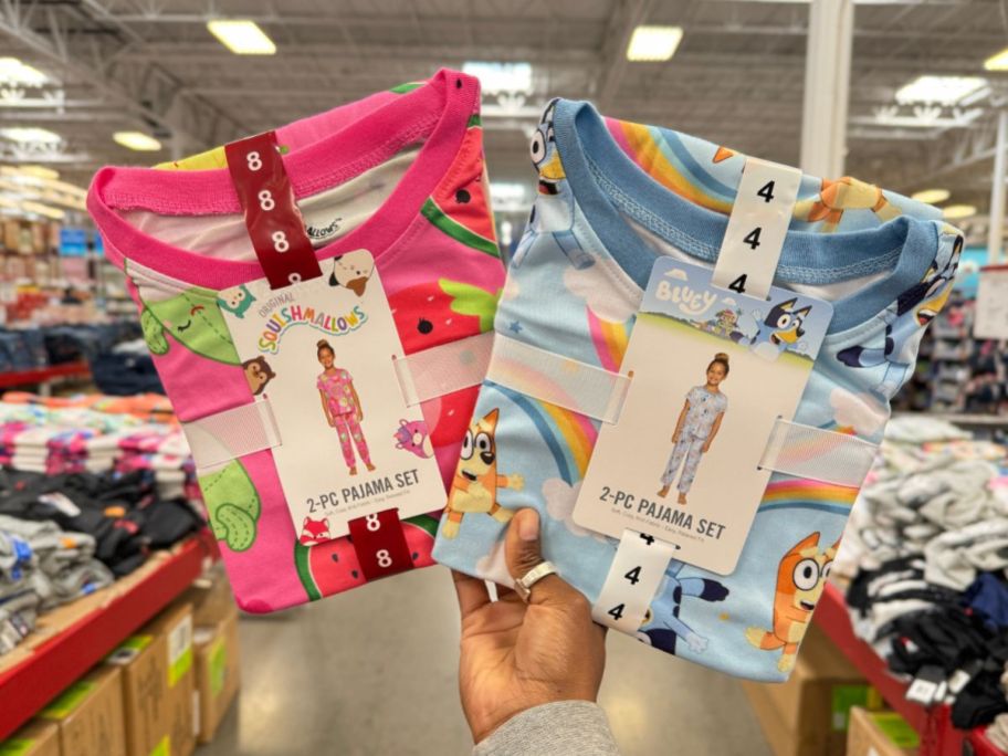A hand holding Squishmallows and Bluey 2-piece Pajama Sets in Sam's Club 