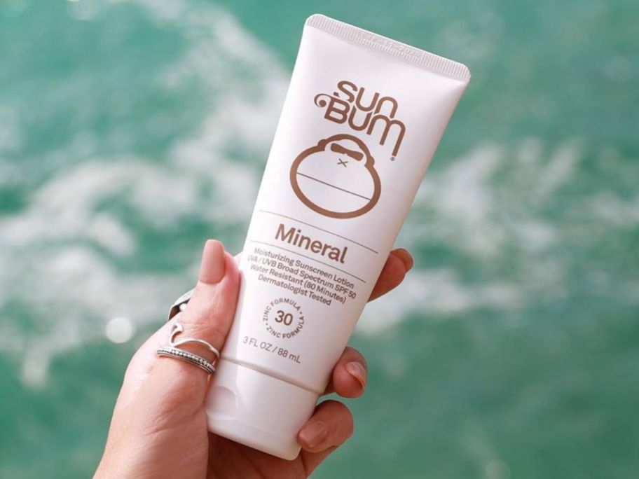Hand holding a tube of Sun Bum Mineral Sunscreen SPF 30