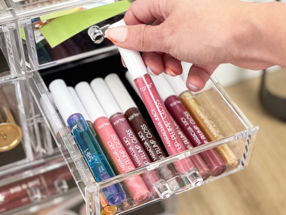 hand grabbing pink Tarte Maracuja Juicy Lip Plump Gloss from clear makeup organizer drawer