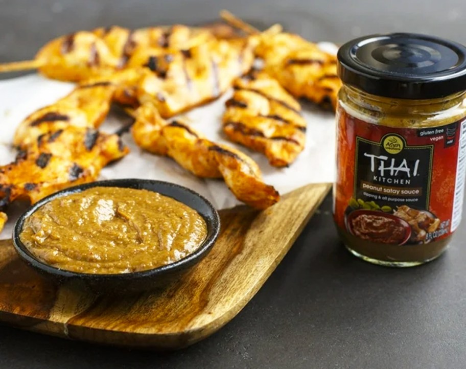 jar of Thai Kitchen Peanut Satay Sauce next to wood board with grilled chicken skewers