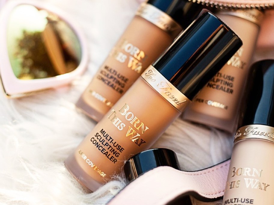 bottles of Too Faced Born This Way Super Coverage Concealer coming out from makeup bag near sunglasses