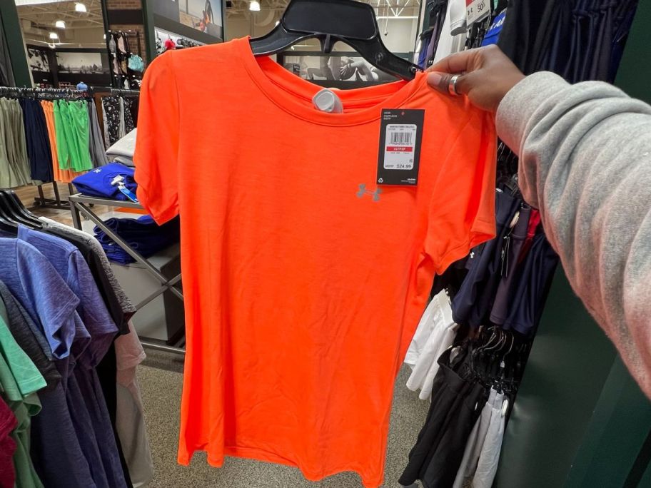 Hand Holding up an orange under armour t-shirt on a hanger