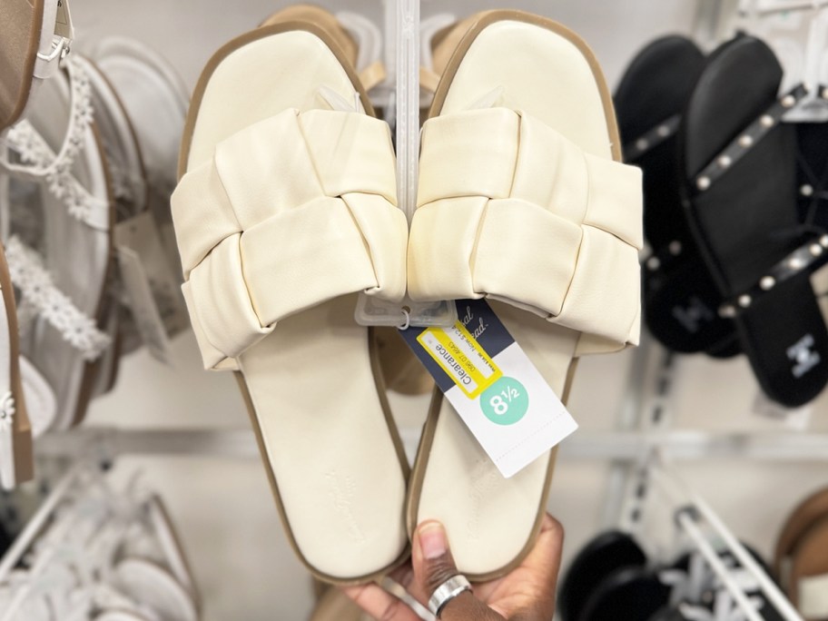 hand holding a white pair of flat sandals at target