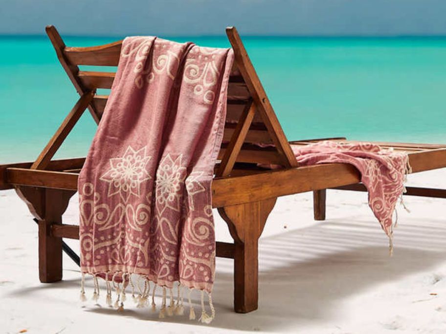 A chaise lounge near the sea with a red Whitley Willows towel on it 