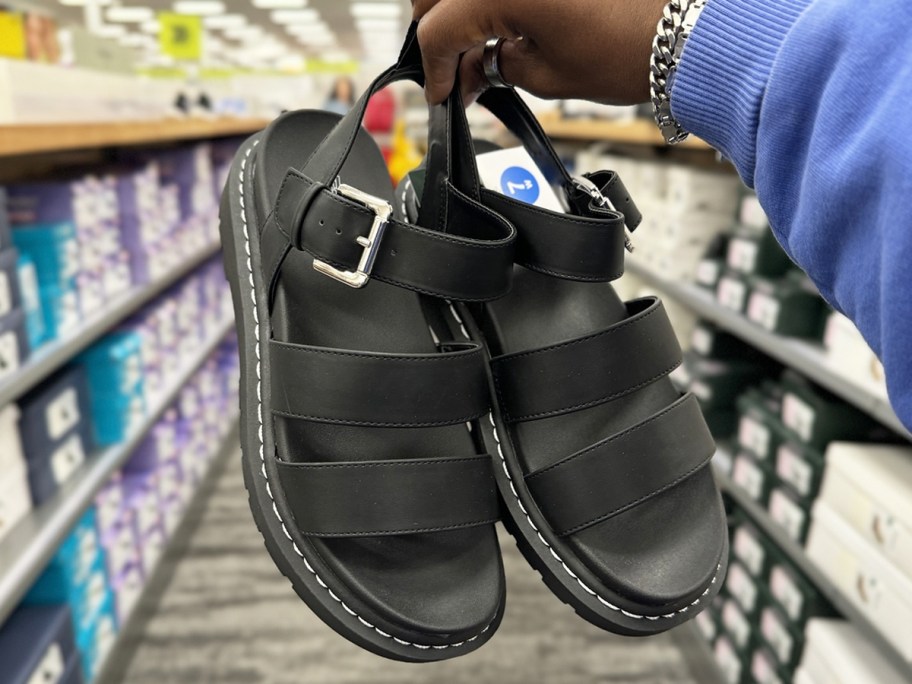 woman holding up a pair of black platform sandals in store
