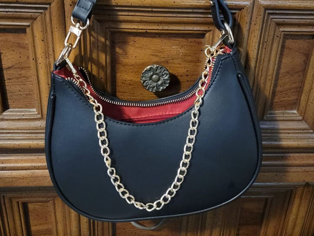 black crescent shaped women's handbag with a gold chain accent hanging from a dresser