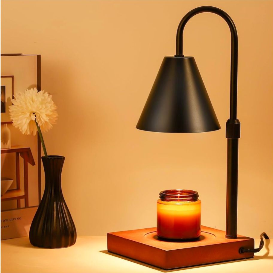 a Candle Warmer Lamp with a black shade sitting on a table warming a candle