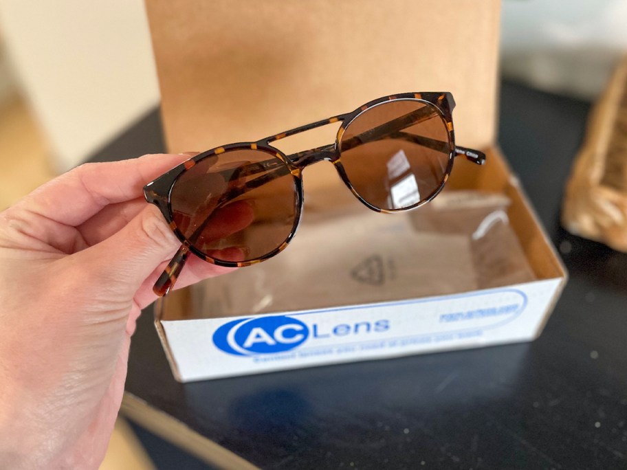 hand holding aclens glasses with box behind it