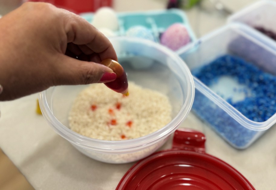 adding drops of yellow food coloring to plastic container with rice inside