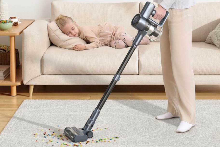 woman using cordless vacuum next to sleeping child