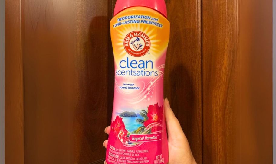 a womans hand holding a 24oz bottle of arm and hammer inwash scent booster in tropical frangrance