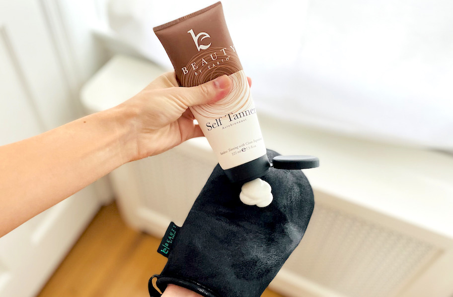 Hand squeezing bottle of beauty by earth self tanner lotion on black mitt