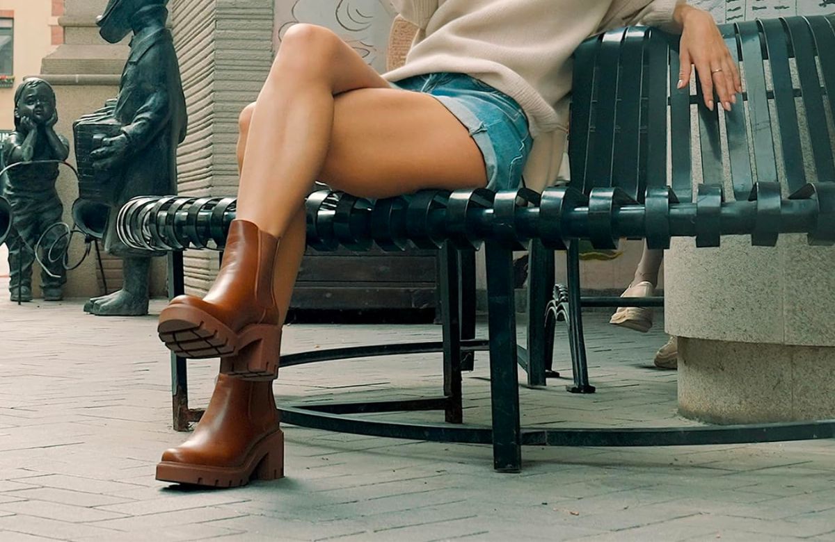 a woman in a pair of brown chelsea boots, sitting on a bench with her legs crossed