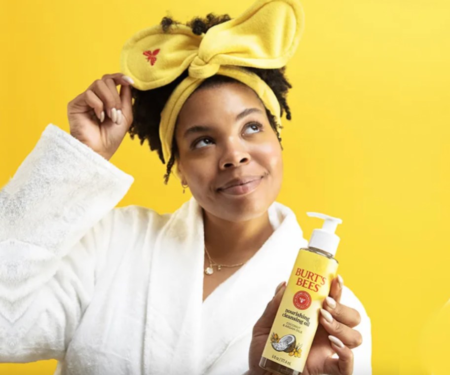 woman in robe and yellow headband holding cleansing oil