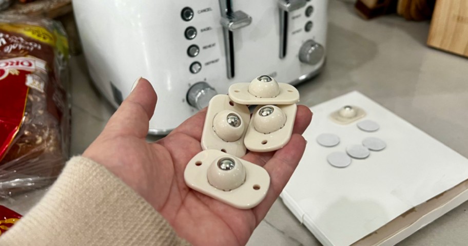 hand holding caster wheels in hand with white toaster in background