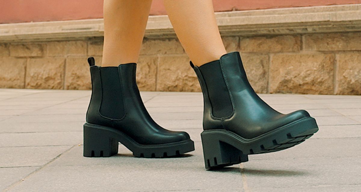 a womens feet in a pair of black PU leather chelsea boots walking on a sidewalk