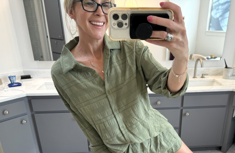 woman taking photo of herself wearing green long sleeve tee and shorts in bathroom