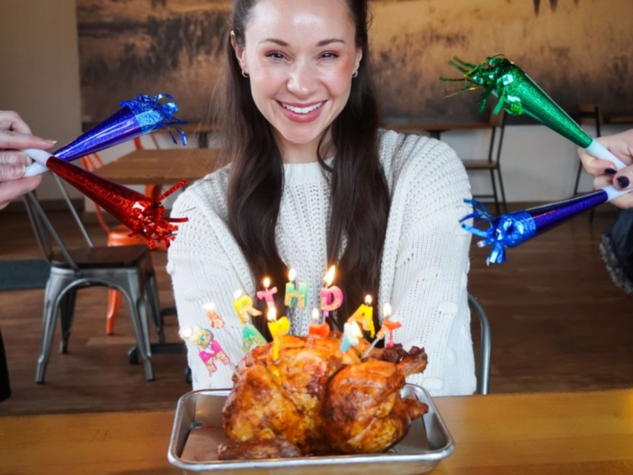 woman sitting in front of rotisserie chicken with birthday candles in it