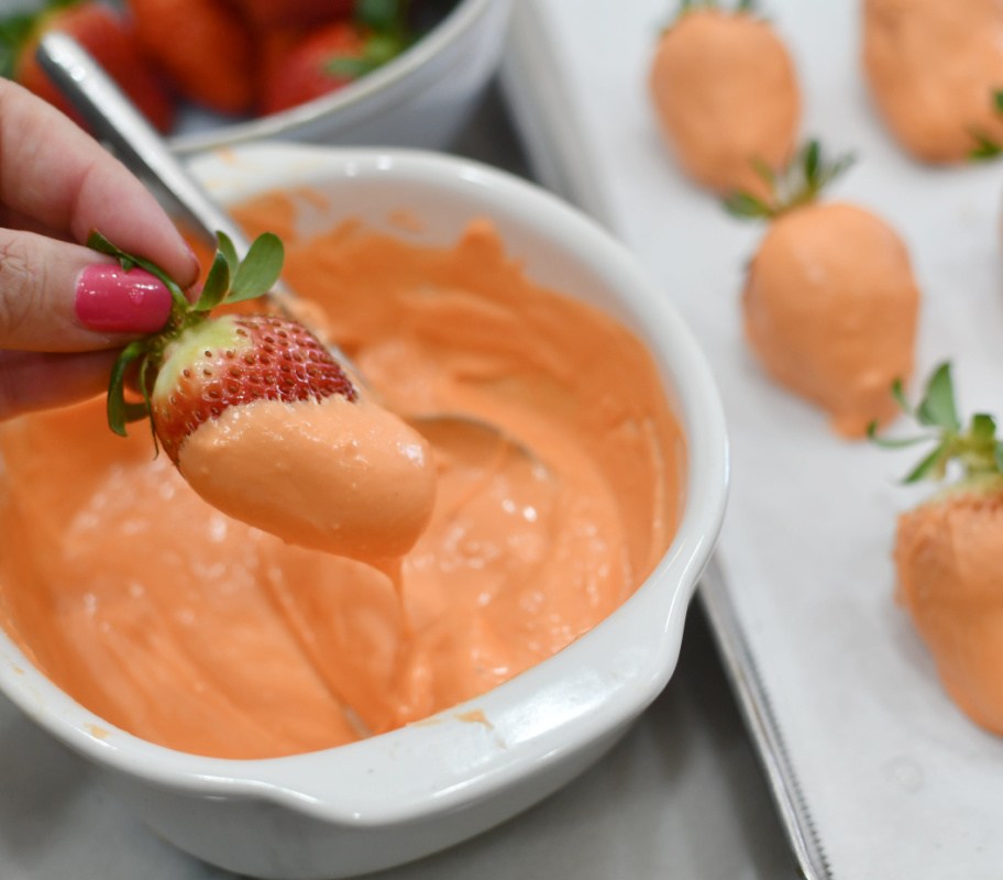 dipping strawberries into orange candy melts