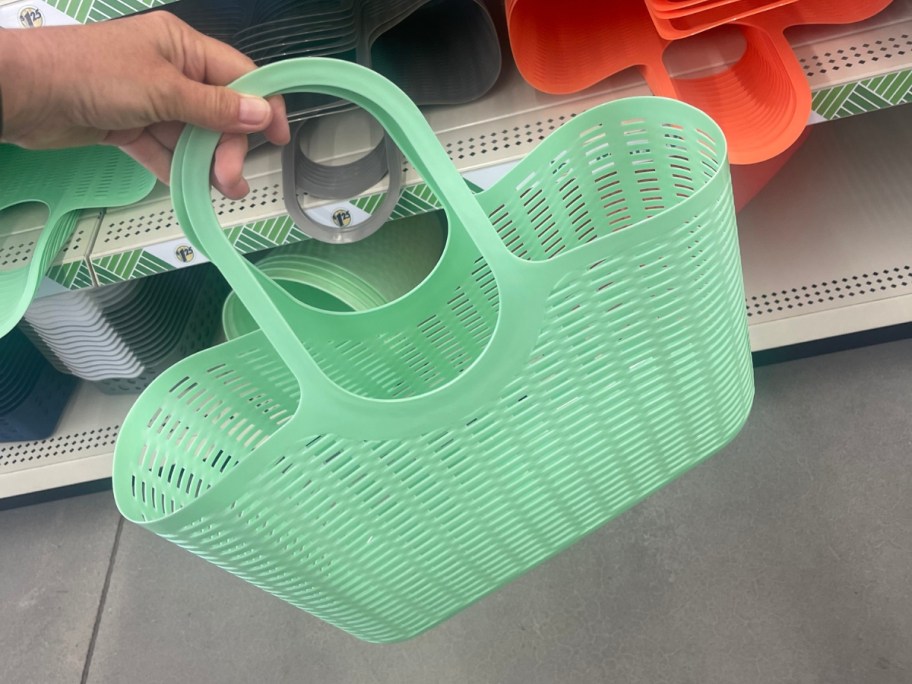 hand holding a light green oval slotted plastic basket with handles