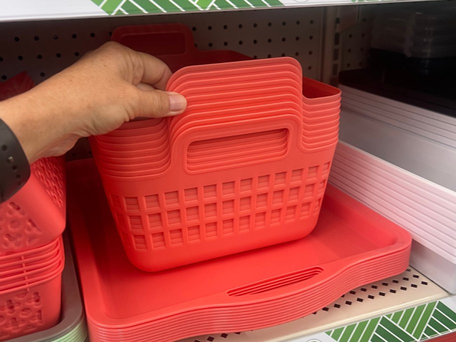 hand reaching for a reddish orange slotted storage basket that's sitting on top of matching trays