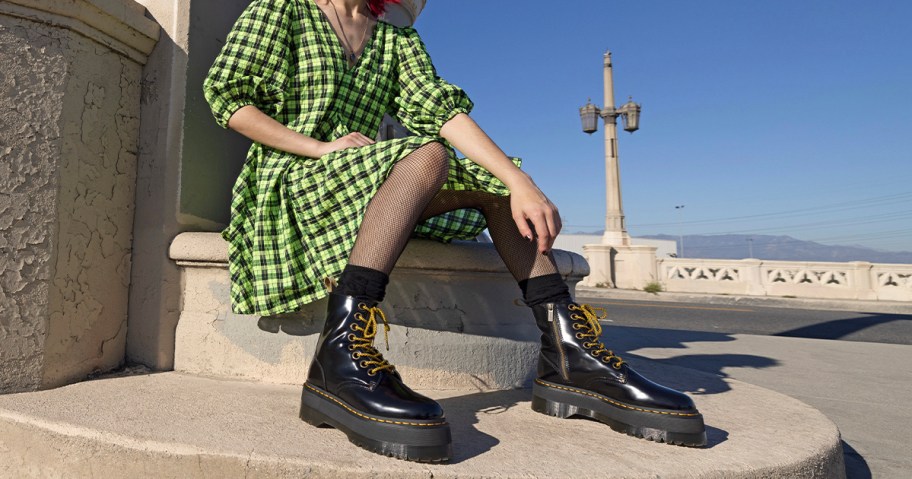 woman in green checkered dress wearing black Dr. Martens boots sitting on steps