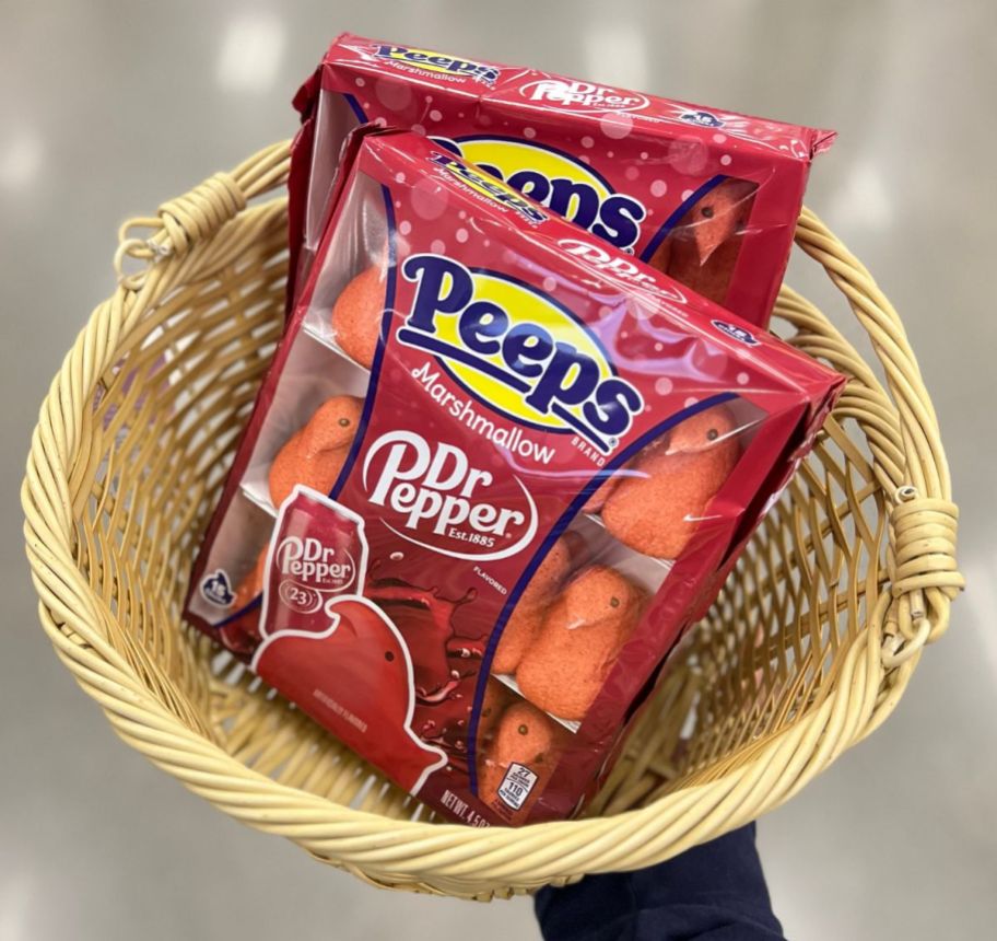 a womans hand displaying a natural colored basket containing 2 packages of dr. pepper flavored peeps