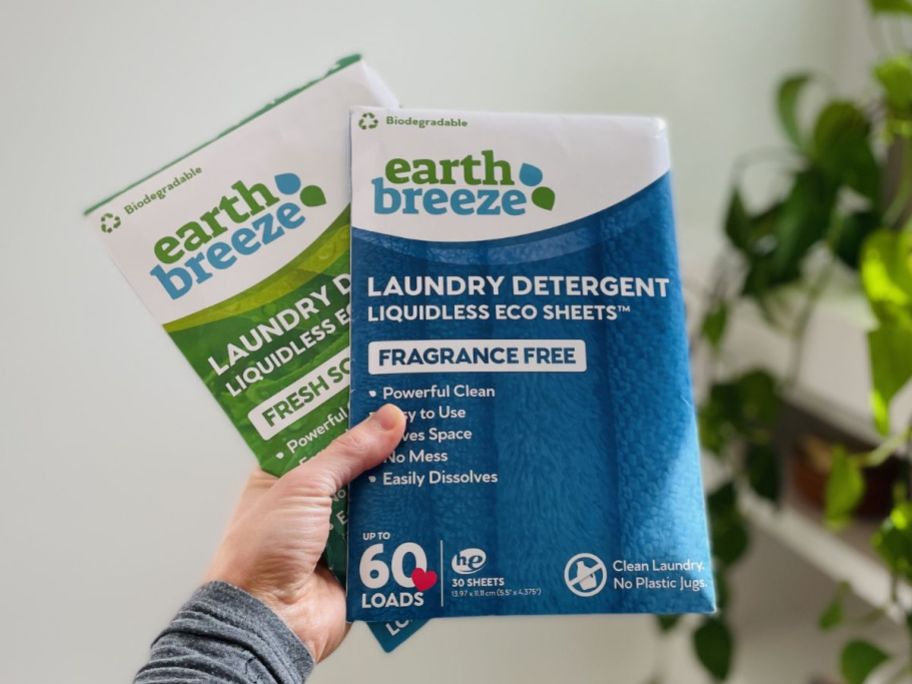 a womans hand holding 2 packages of earth breeze laundry det in scented and unscented.