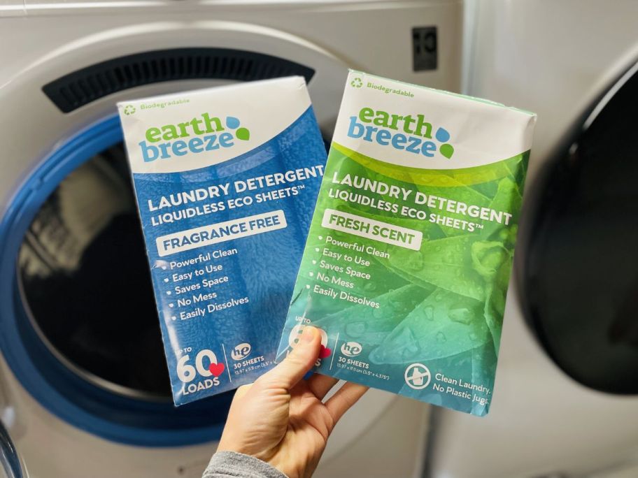 a womans hand holding 2 packages of earth breeze laundry det in scented and unscented. 
