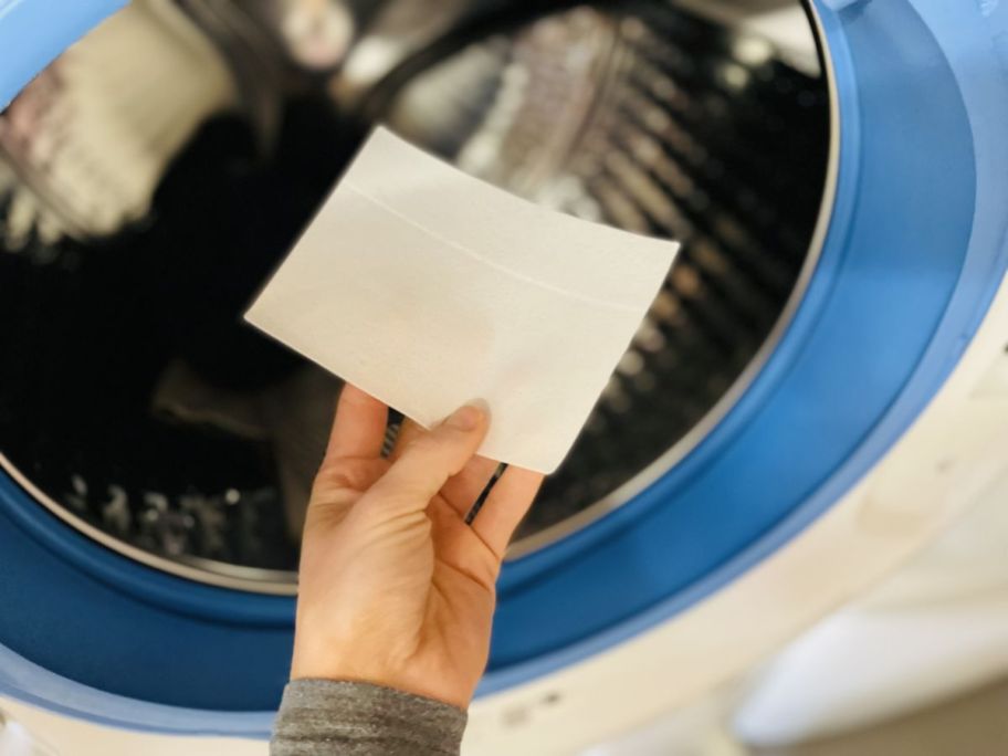 womans hand placing a sheet of earth breeze laundry det into a front loading washer