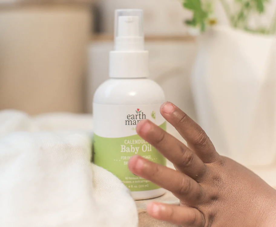 baby hand reaching for bottle of earth mama baby oil