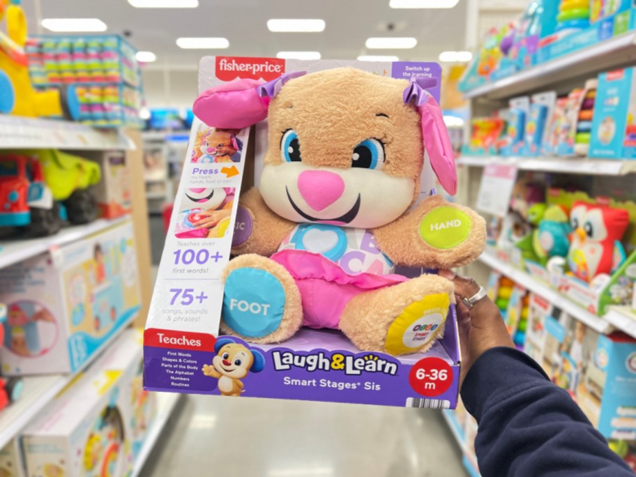 hand holding a fisher price laugh and learn sis puppy in packaging in a store aisle