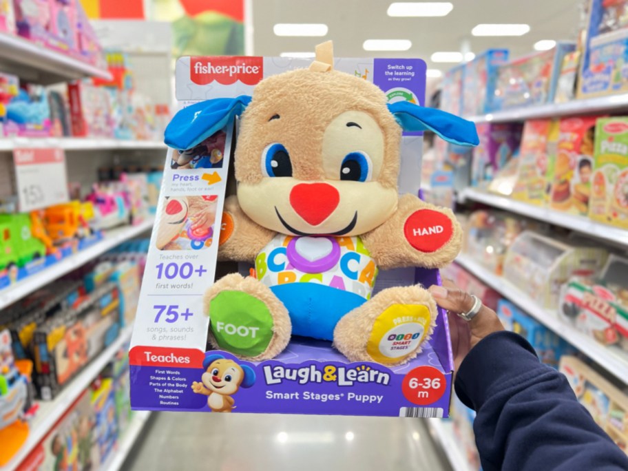 hand holding up a fisher price laugh and learn puppy in the package in a store aisle