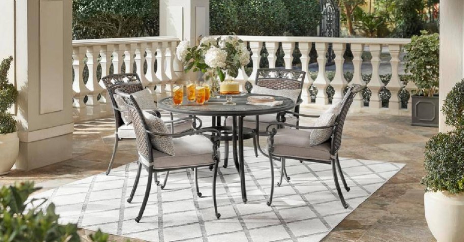 five piece patio set displayed on a rug with table and flowers on it