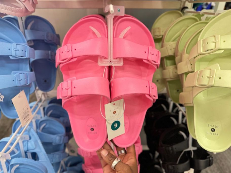 a pair of pink footbed sandals on a peg in a store in between a blue pair and green pair