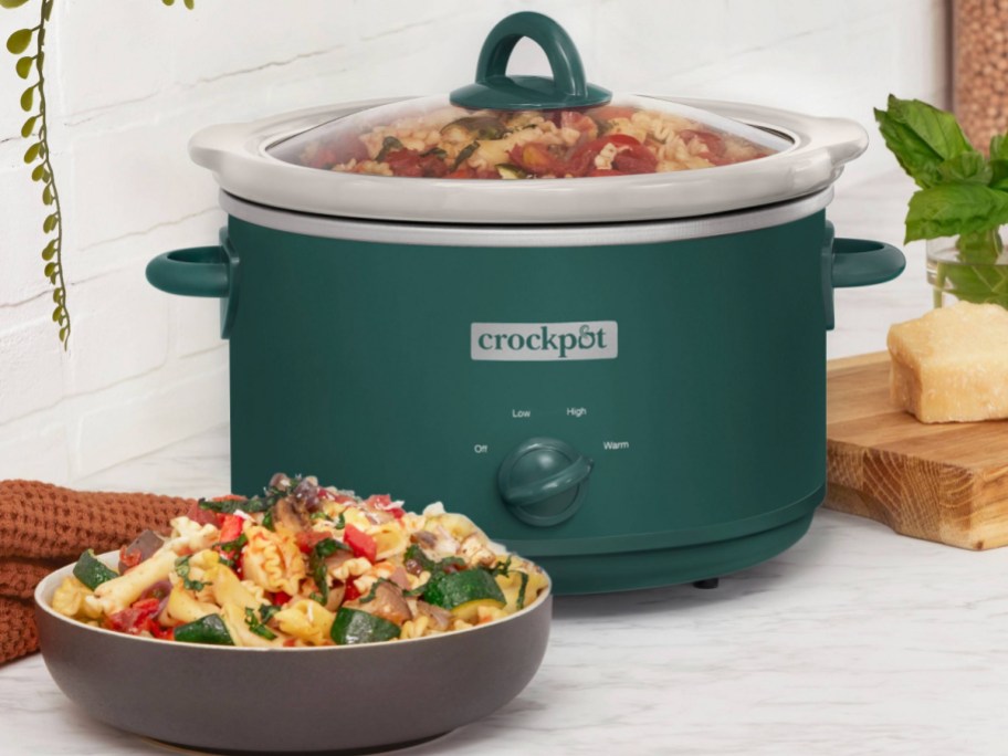 green crockpot displayed with a bowl of food next to it