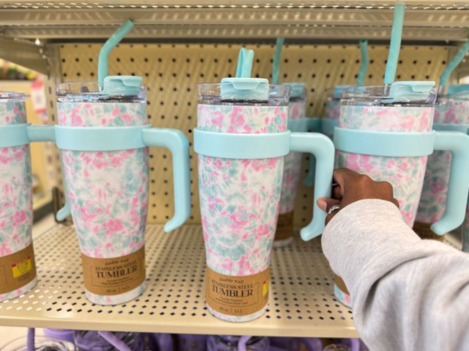 hand touching a 40 oz pink, blue and white stainless steel straw tumbler on shelf at Hobby Lobby