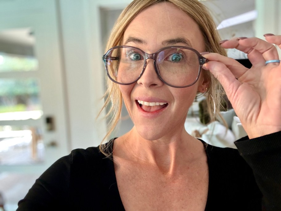 smiling woman looking at the camera while touching the edge of her glasses