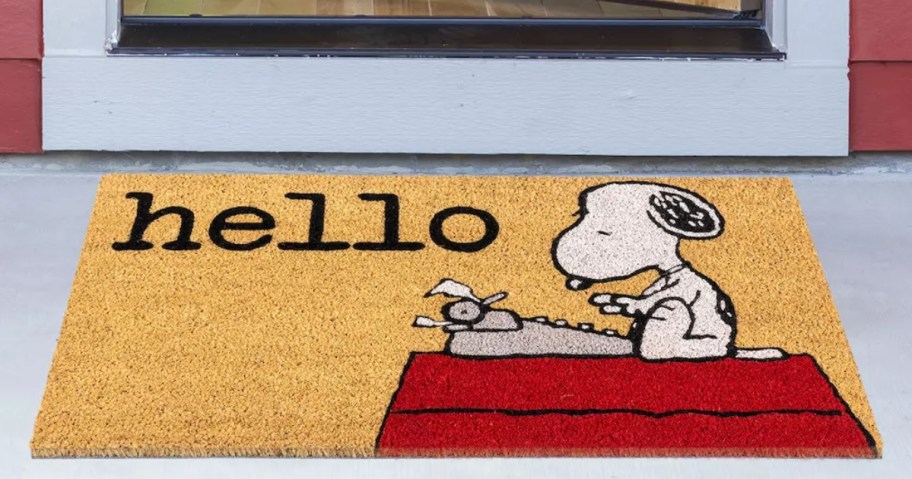 coir doormat in front of a door with Snoopy typing on a typewriter sitting on his red doghouse