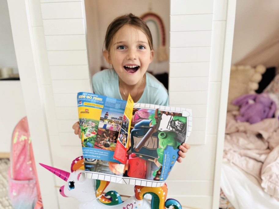 girl in a playhouse holding open a lego magazine