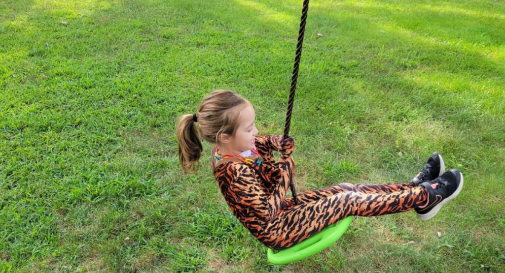 little girl sitting on swing disc with rope playing outside