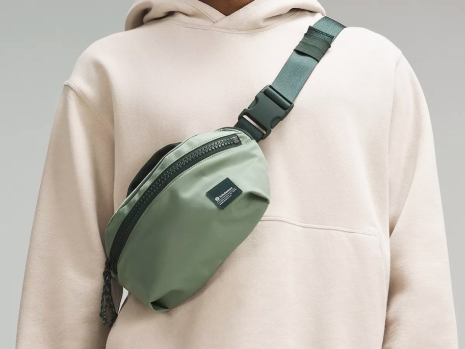 person in cream colored hoodie wearing a green belt bag across their chest