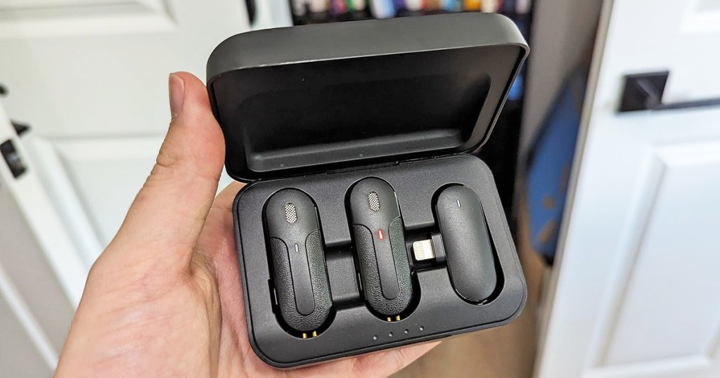 hand holding a set of clip-on microphones and receiver in black charging case