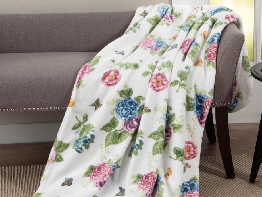 white throw blanket with blue and pink flowers and butterflies laying over a grey couch